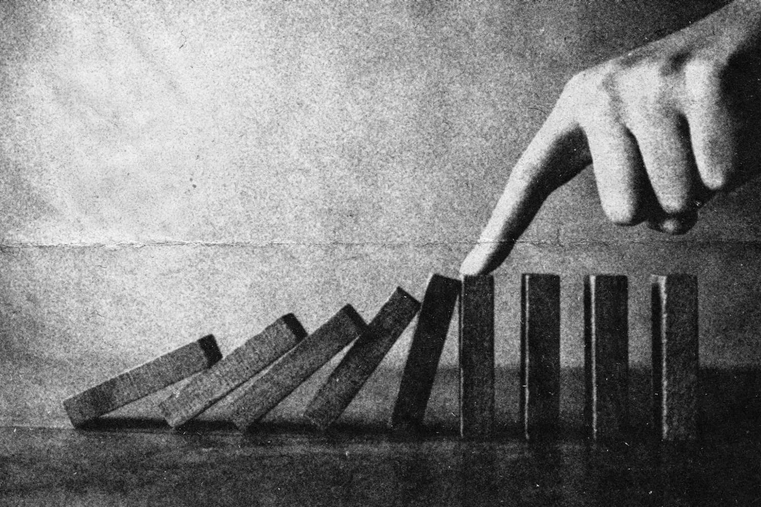 A finger stopping a row of falling dominoes